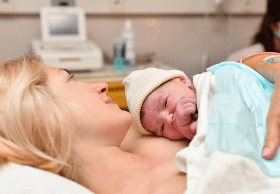 mother laying down and holding newborn baby in hospital