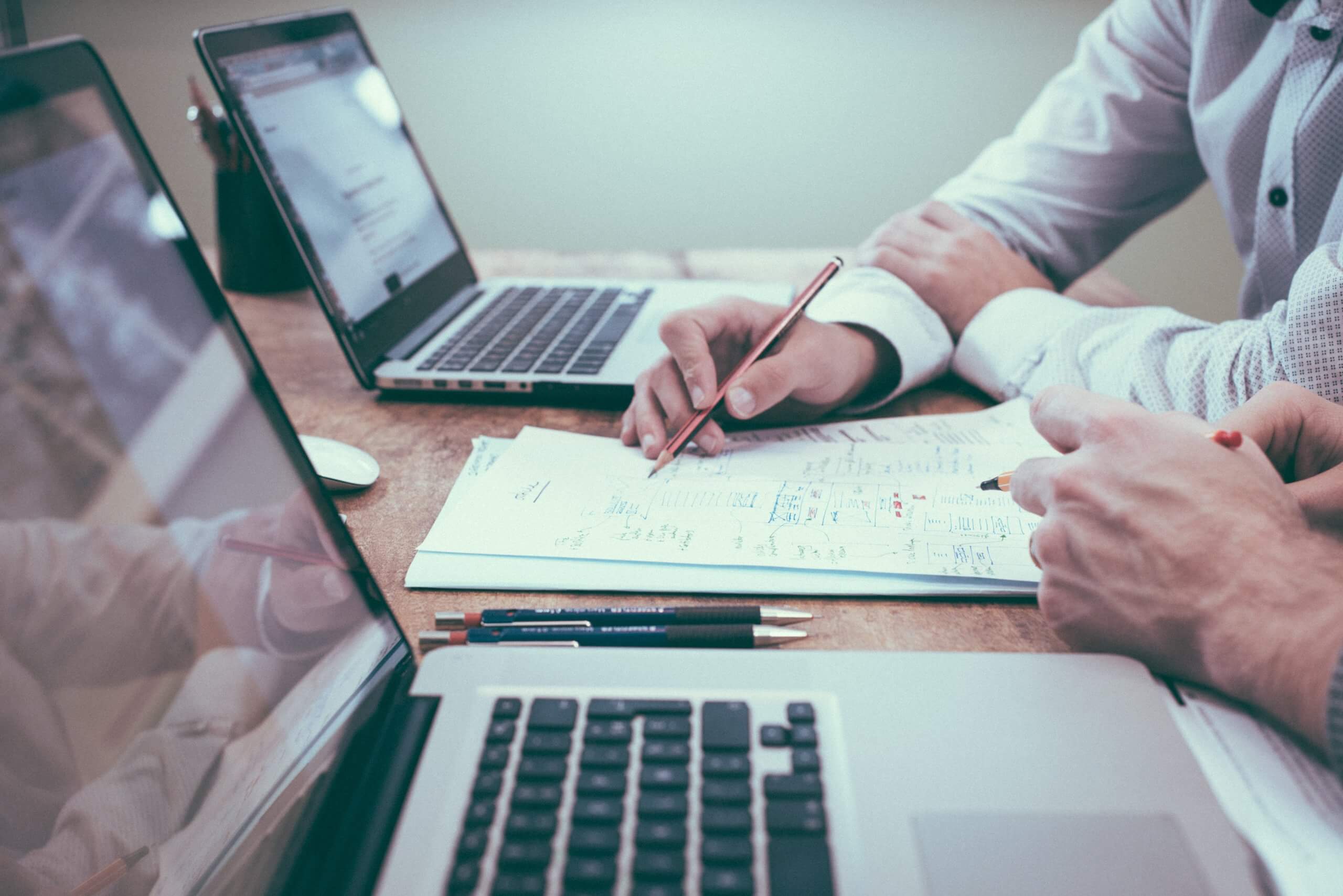 two people working together with their own macbooks and some papers in between them