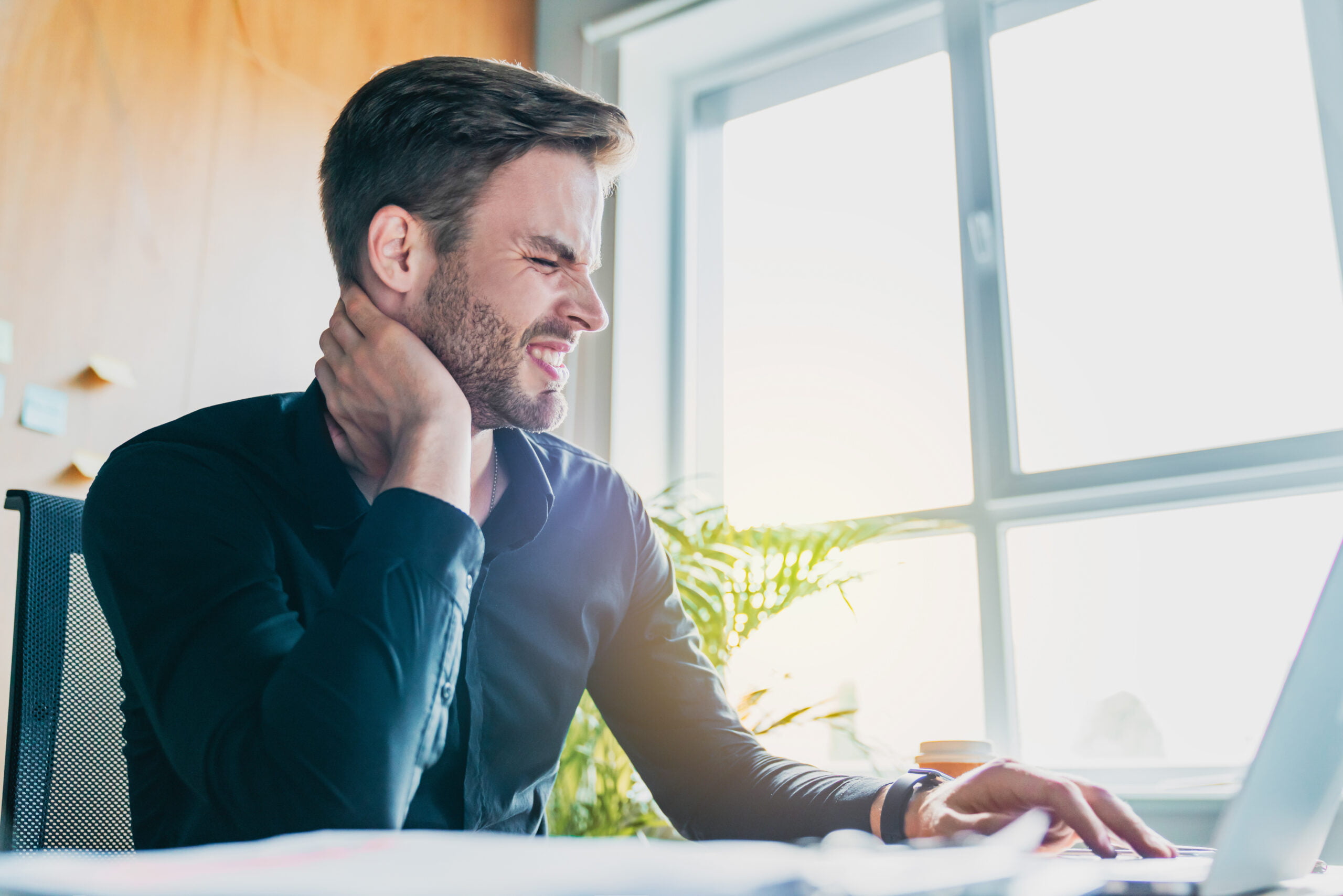 Young businessman holding sore neck while using laptop computer indoor in Maryland