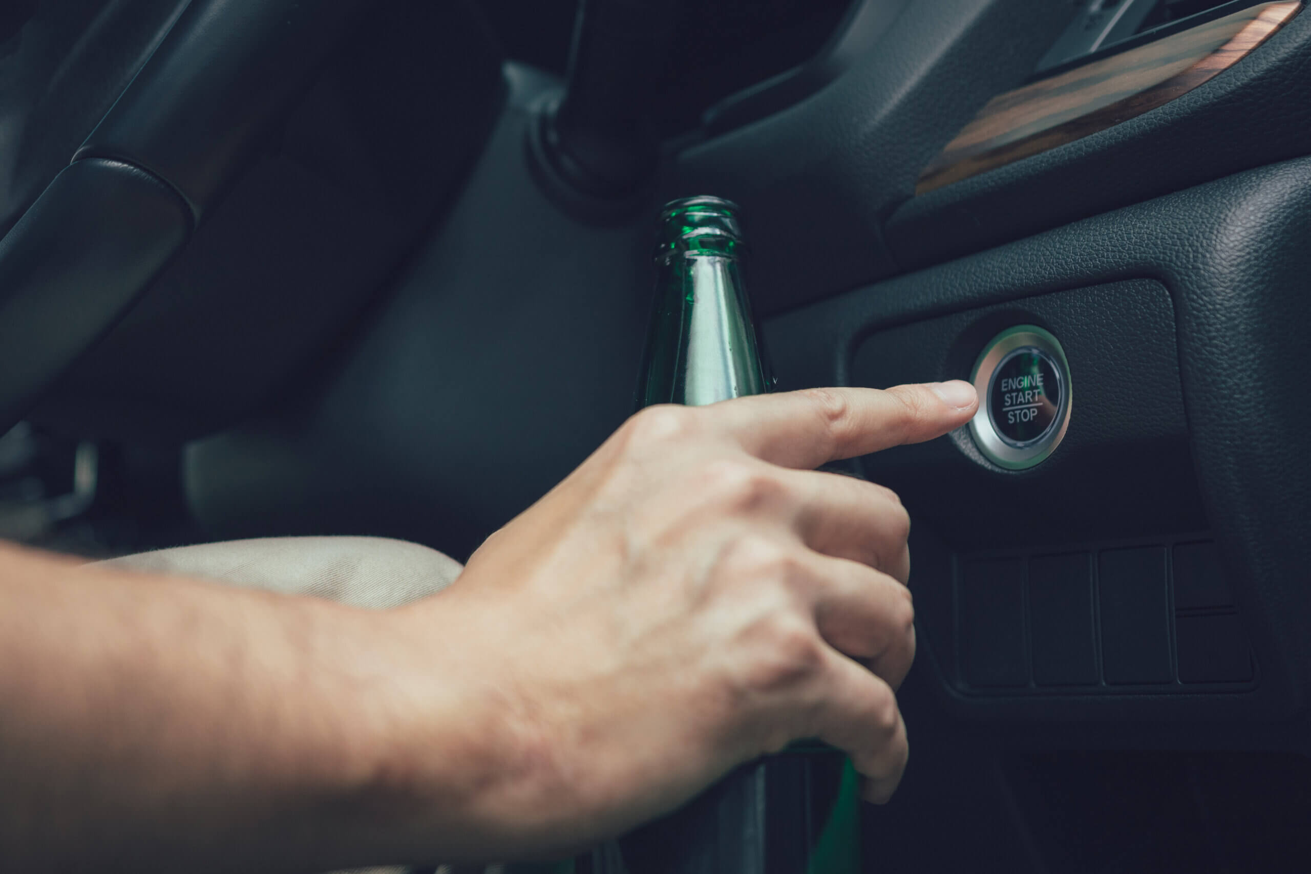 The man hand is holding a beer bottle and pressing the engine start button. DUI attorney in Baltimore