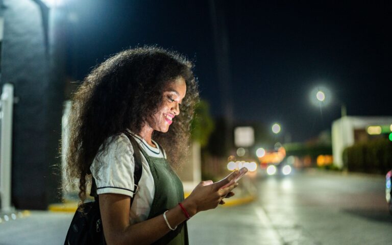 uber crash data can help your personal injury case. Woman waits for her uber at night while checking the app on her phone.
